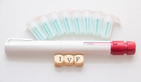 Αυτόματο στυλό ένεσης IVF με φιαλίδια ορμονών τοποθετημένα σε σειρά και ξύλινα τουβλάκια που σχηματίζουν τη λέξη IVF.