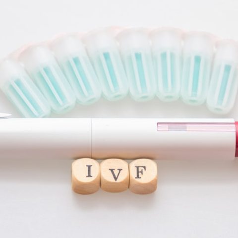 Αυτόματο στυλό ένεσης IVF με φιαλίδια ορμονών τοποθετημένα σε σειρά και ξύλινα τουβλάκια που σχηματίζουν τη λέξη IVF.